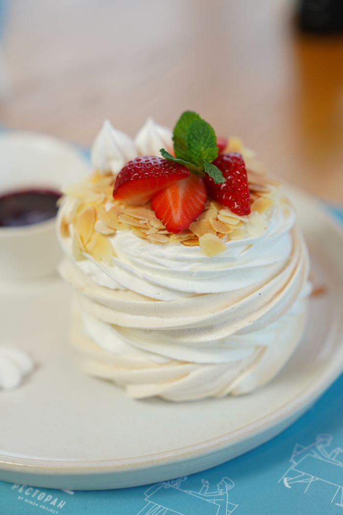 Close-up of a pavlova dessert topped with fresh strawberries and mint, on a plate.