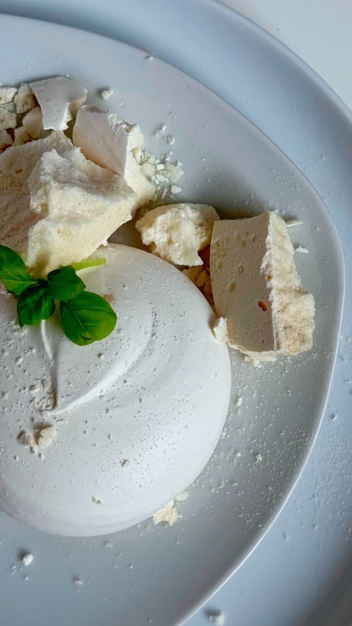 A detailed shot of a white meringue dessert garnished with fresh basil leaves on a white plate.